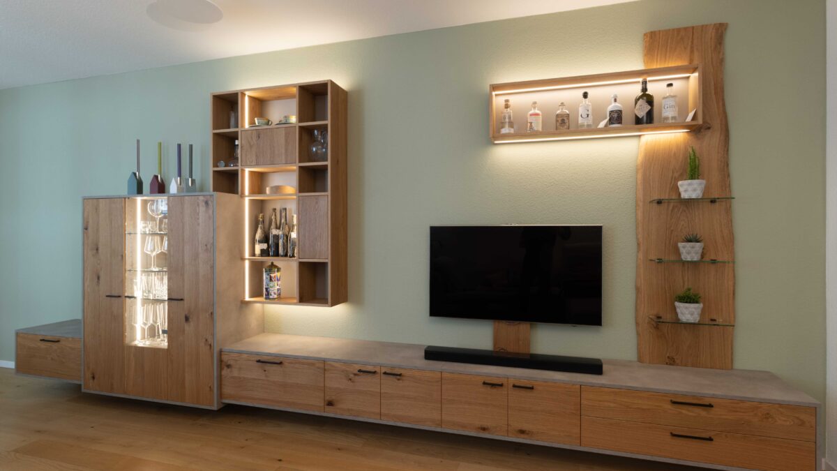 Schreinermöbel in Eiche, schwarzen Griffen, Beton-Optik und variabler LED-Beleuchtung vor salbeigrün gestrichener Wand