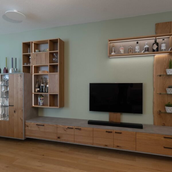 Schreinermöbel in Eiche, schwarzen Griffen, Beton-Optik und variabler LED-Beleuchtung vor salbeigrün gestrichener Wand